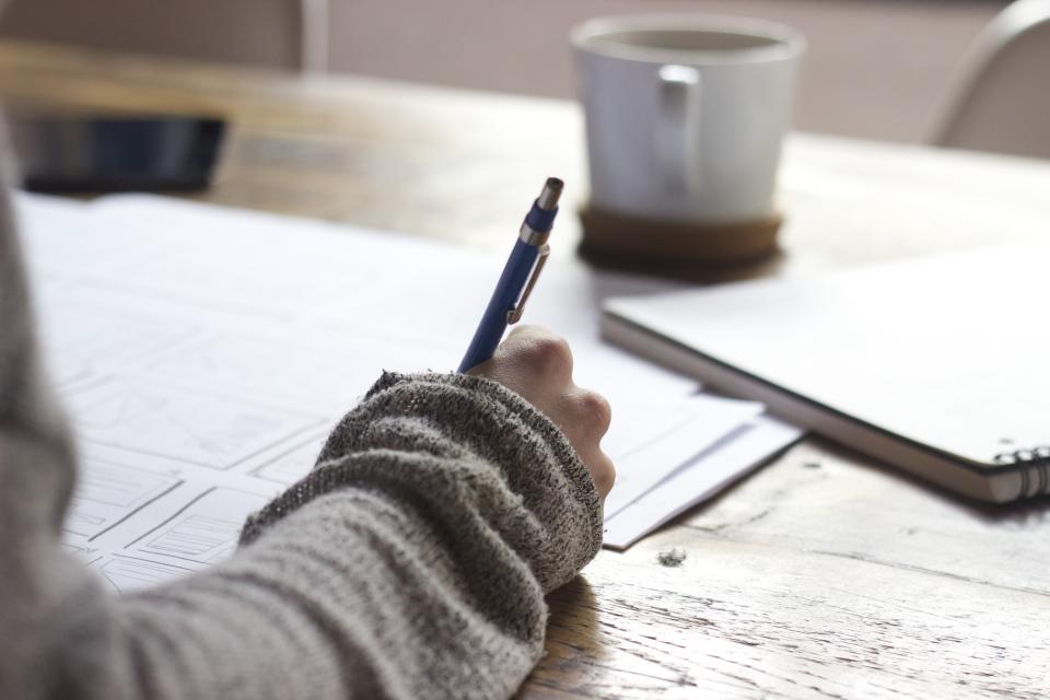 A student working through math problems by hand at a desk with a notebook and coffee.
